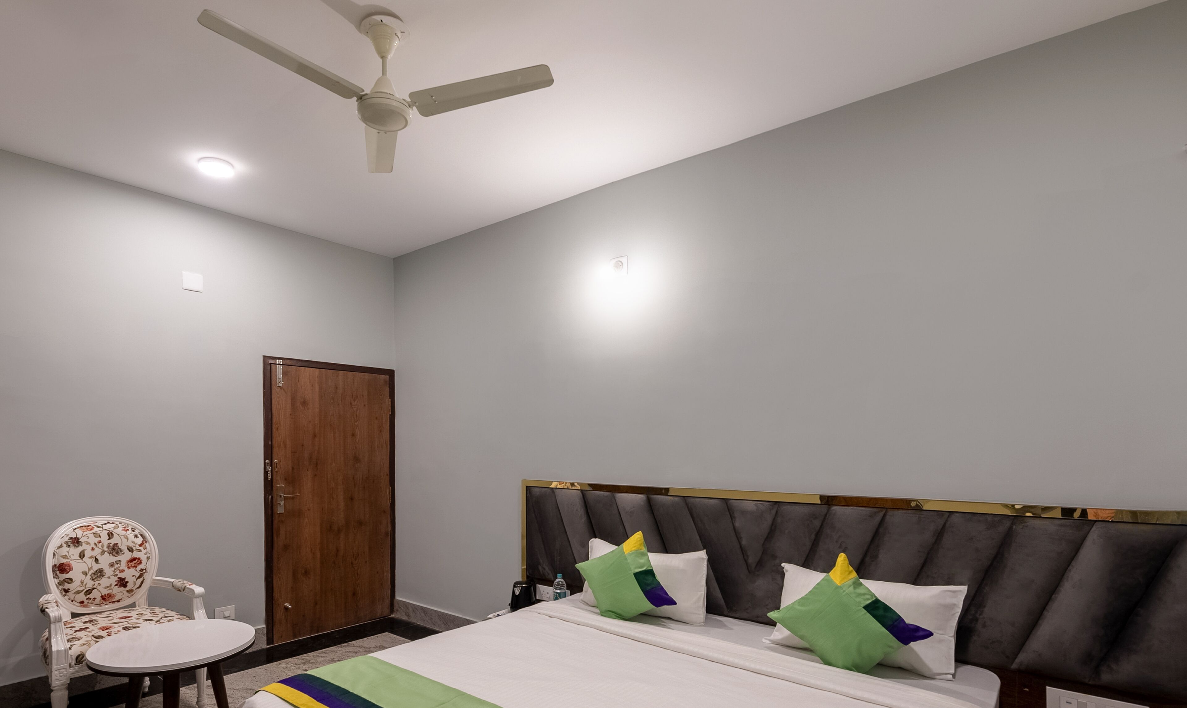 A hotel room with a bed, a chair, a ceiling fan, and a door.