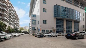A parking lot with multiple cars and a modern building with large windows and balconies. - Vienna Classic Hotel （ ZhanJiang coastal park sea view gallery hotel ） (Zhanjiang)