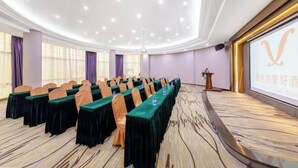 A conference room with rows of tables and chairs, a podium, and a projection screen with a logo. - Vienna Classic Hotel （ ZhanJiang coastal park sea view gallery hotel ） (Zhanjiang)