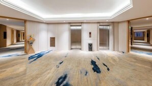 A spacious hotel lobby with a modern design, featuring a central elevator, a reception desk, and a patterned floor. - Vienna Classic Hotel （ ZhanJiang coastal park sea view gallery hotel ） (Zhanjiang)