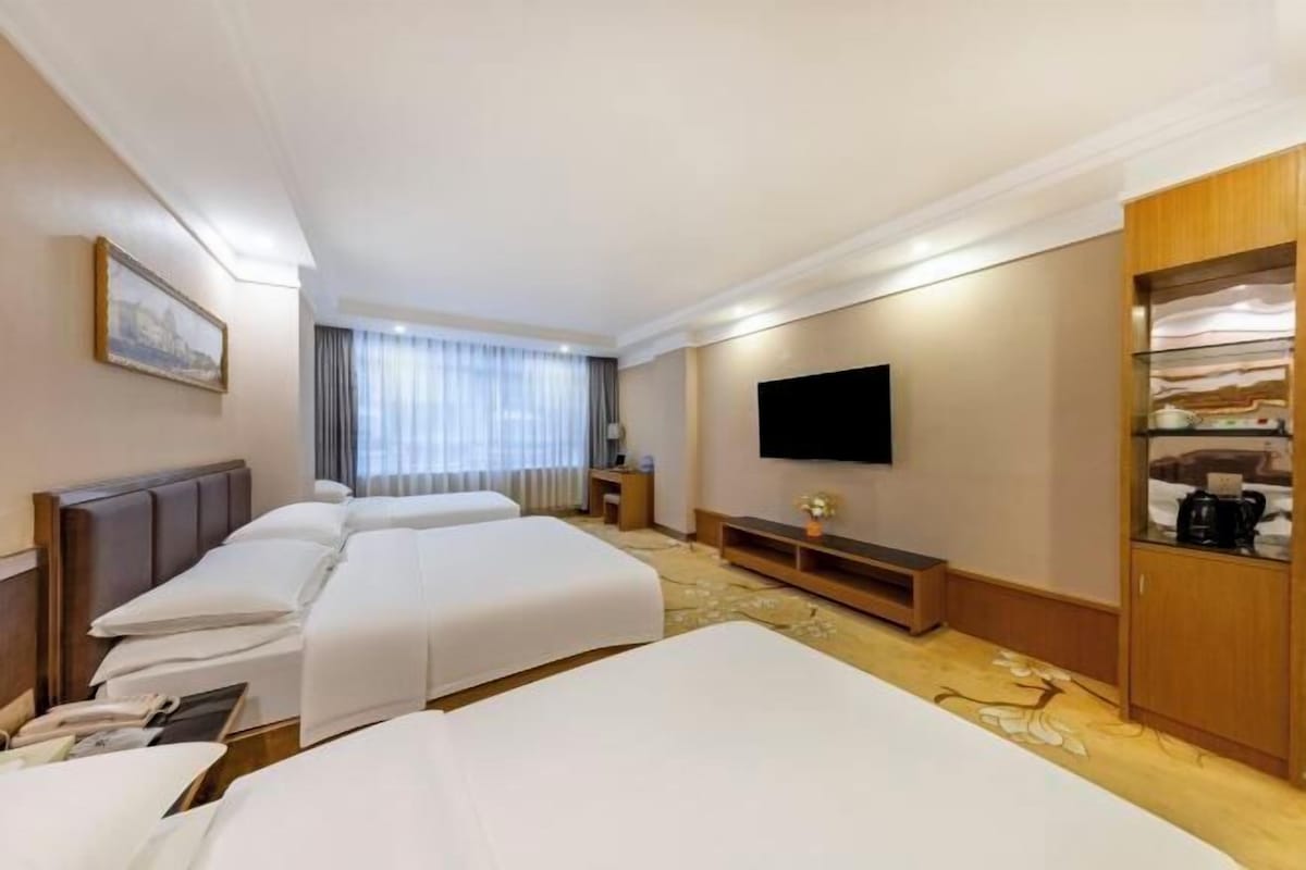 Habitación de hotel con tres camas, televisión de pantalla plana, cafetera y estantería.
