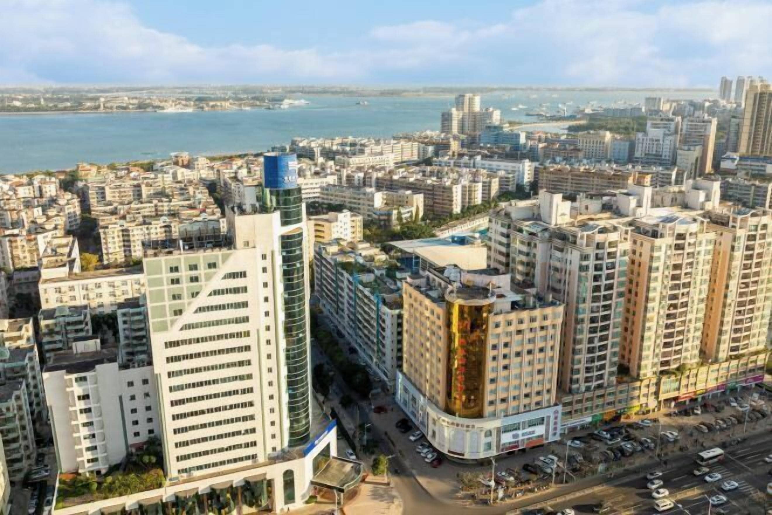 Un quartier urbain caractérisé par de nombreux immeubles de grande hauteur, une vue sur le front de mer et une rue animée où circulent de nombreux véhicules.