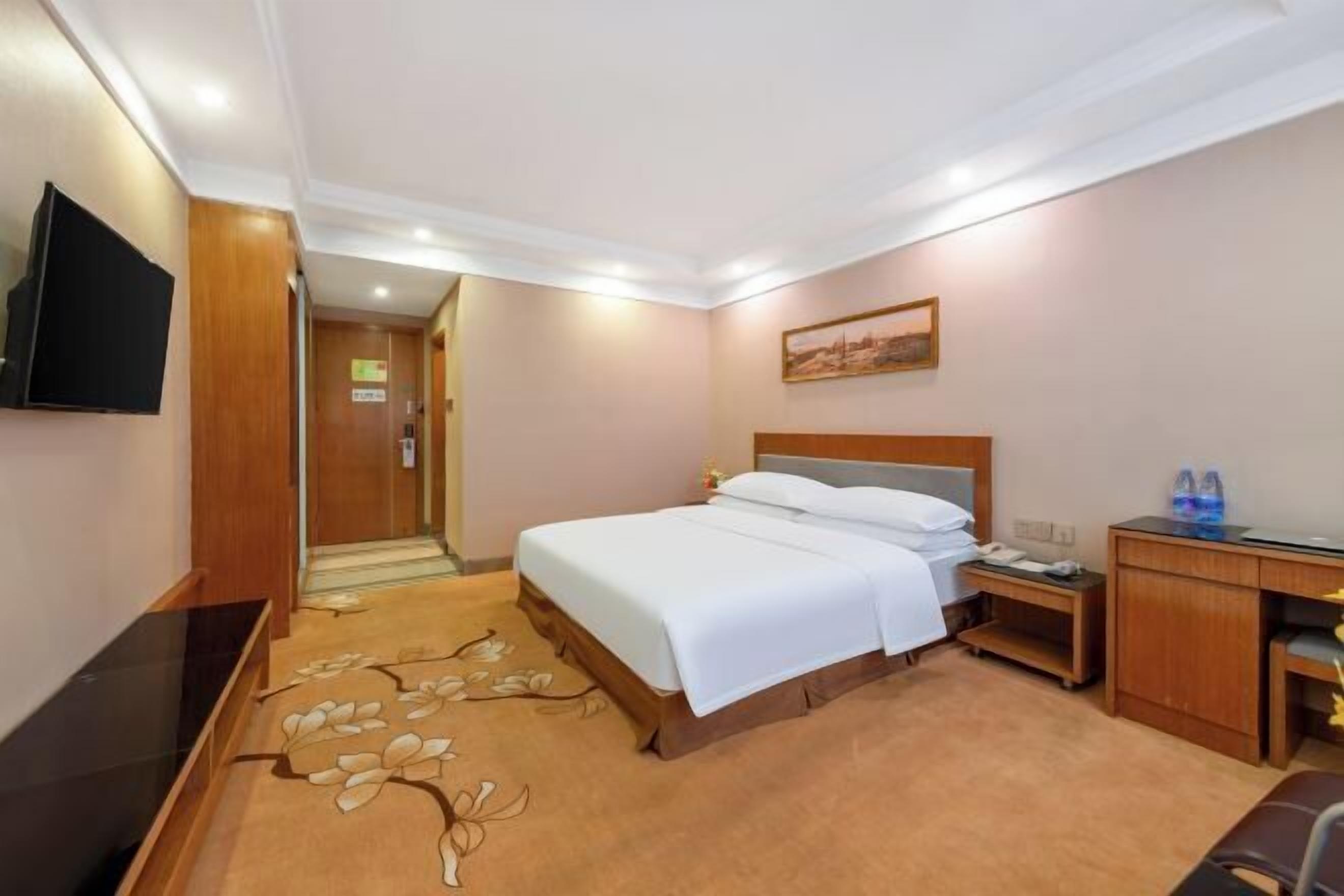 A hotel room with a bed, bedside table, desk, and a television mounted on the wall.