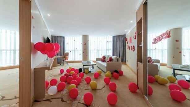 A modern hotel room with a large window, a sofa, a coffee table, and a carpet with scattered balloons. - Vienna Classic Hotel （ ZhanJiang coastal park sea view gallery hotel ） (Zhanjiang)