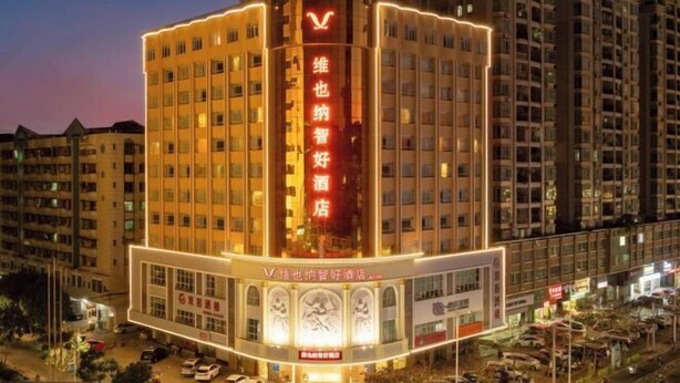A hotel with a prominent red sign, multiple floors, and a well-lit entrance. - Vienna Classic Hotel （ ZhanJiang coastal park sea view gallery hotel ） (Zhanjiang)
