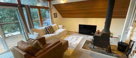 A living room with a brown sofa, a flat-screen TV, and a wood-burning stove.