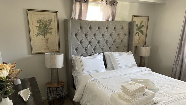 A neatly made bed with white linens, a bedside table with a lamp, and framed botanical artwork on the walls.