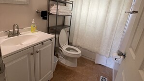 A bathroom with a white sink, a toilet, a shelf with towels, and a shower curtain.