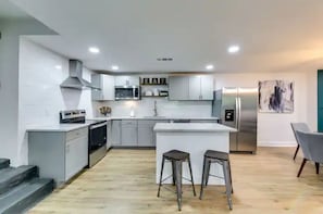 A modern kitchen with white cabinets, a central island, bar stools, and a stainless steel refrigerator.