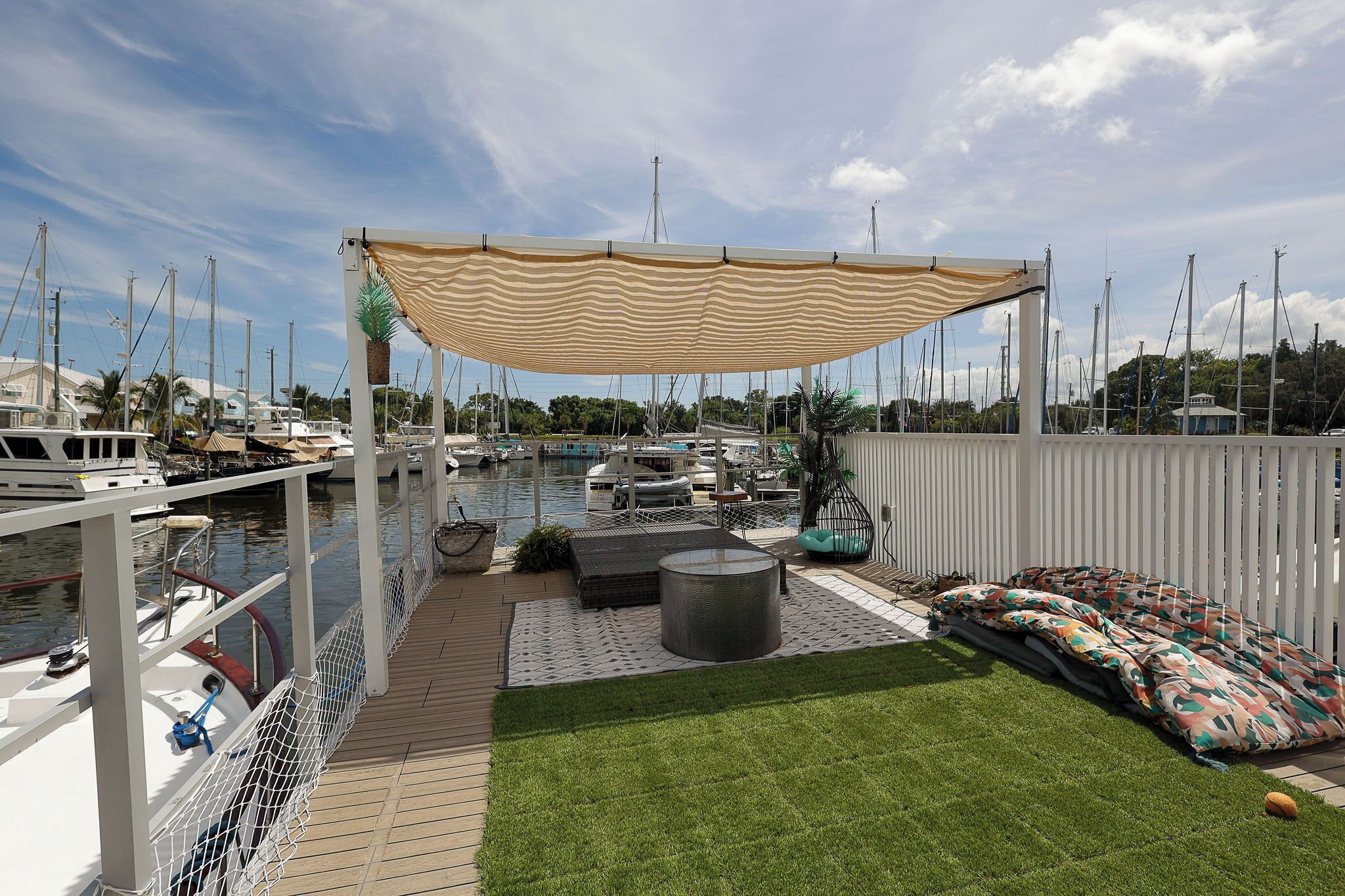 Un puerto deportivo con barcos amarrados, una zona de estar cubierta con cojines y una terraza con césped.
