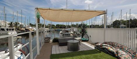 Un puerto deportivo con barcos amarrados, una zona de estar cubierta con cojines y una terraza con césped.