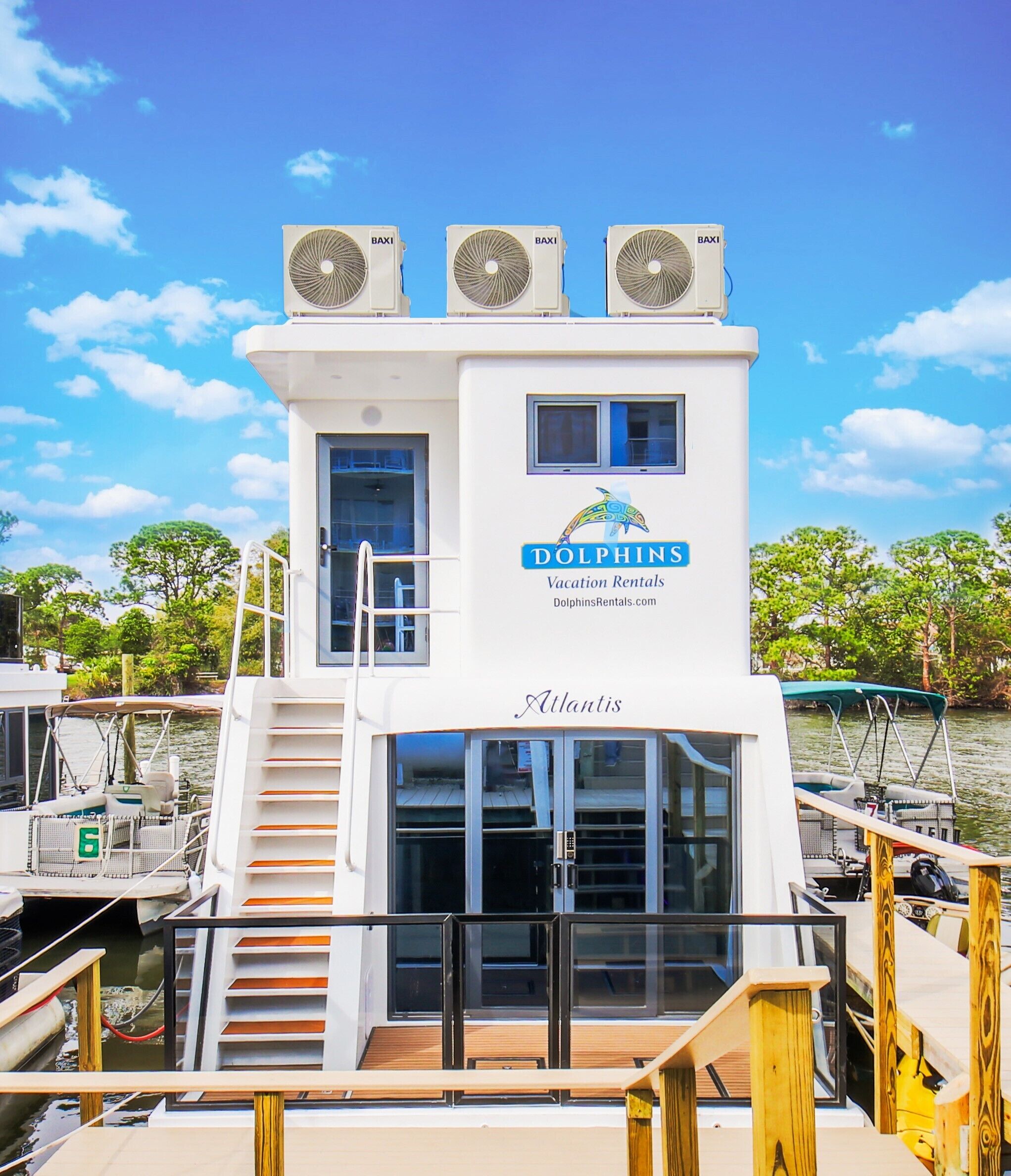 A white boat with three Baxi air conditioning units, a Dolphin's Vacation Rentals logo, and a nameplate reading "Atlantis".