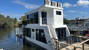 A white houseboat docked at a marina with a covered deck and a small upper deck with two fans. - Dolphins Vacation Rental  (Merritt Island)