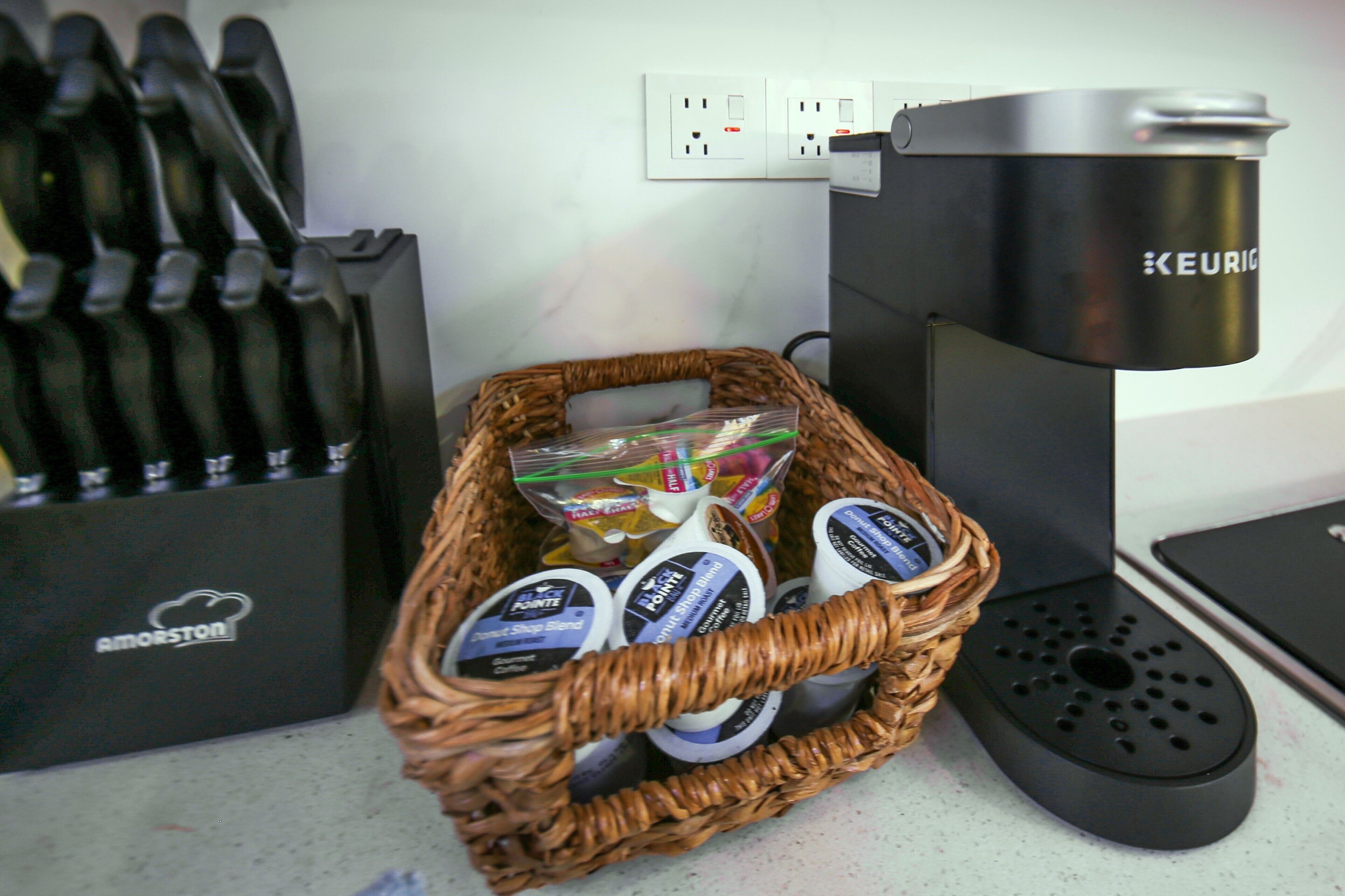 Un plan de travail de cuisine avec une machine à café, un panier de dosettes de café et un bloc à couteaux.
