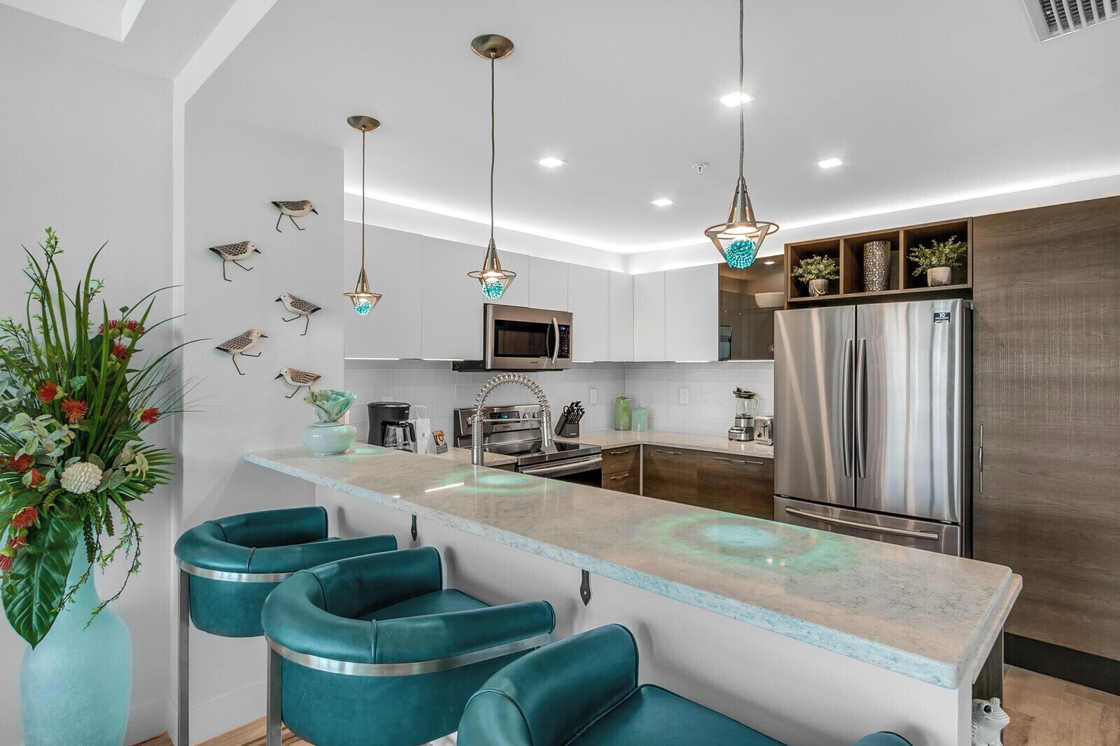 Cozinha moderna com ilha central, eletrodomésticos de aço inoxidável e banquetas de bar cor turquesa.