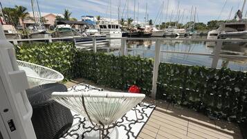 Un port de plaisance avec des bateaux, une clôture blanche et un espace patio aménagé avec des chaises en osier et un tapis à motifs.