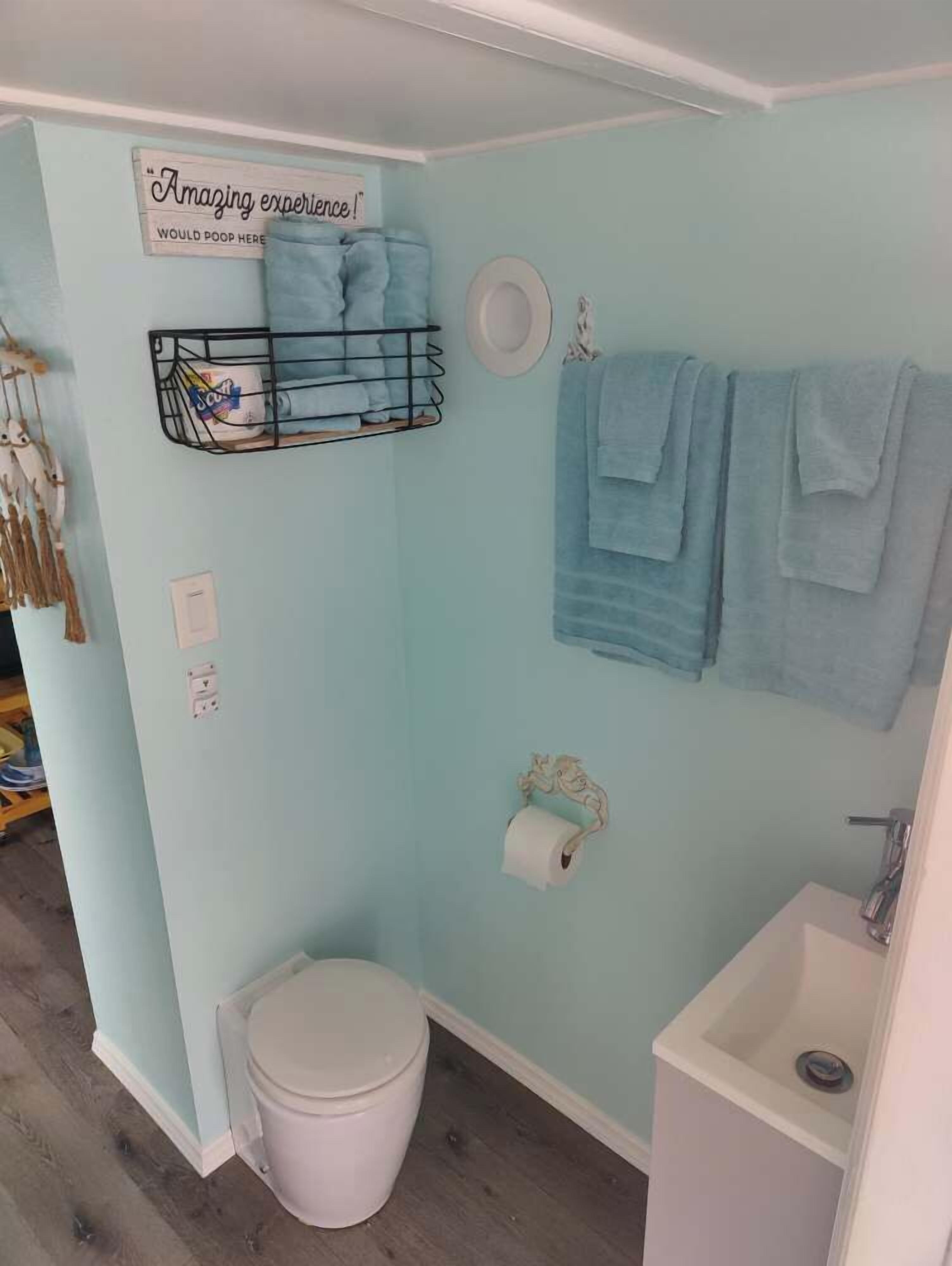 A bathroom with a light blue wall, a white toilet, a sink, and a towel rack with towels.