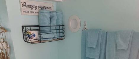A bathroom with a light blue wall, a white toilet, a sink, and a towel rack with towels.