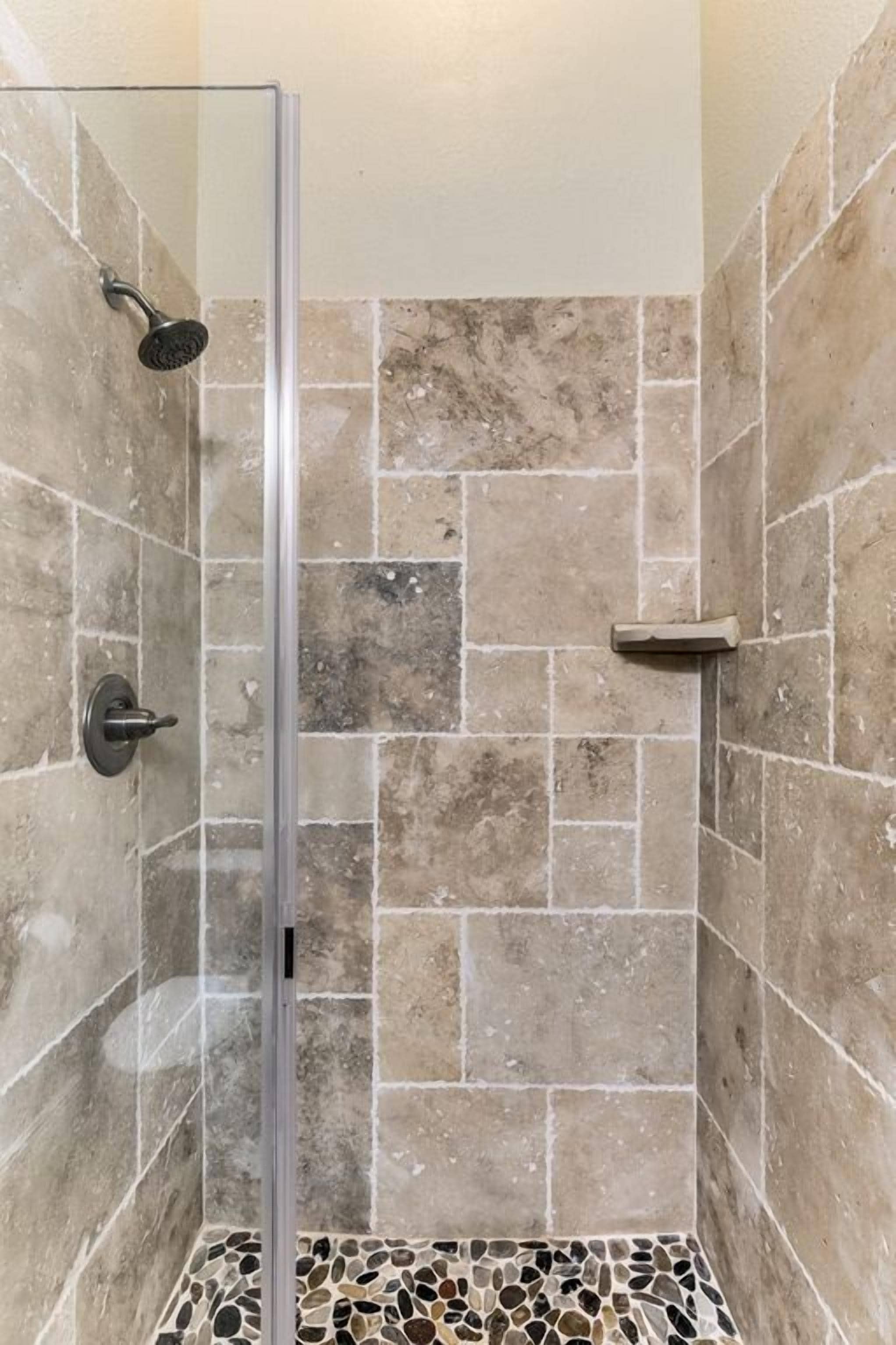 A glass-enclosed shower with a handheld showerhead and a wall-mounted control.