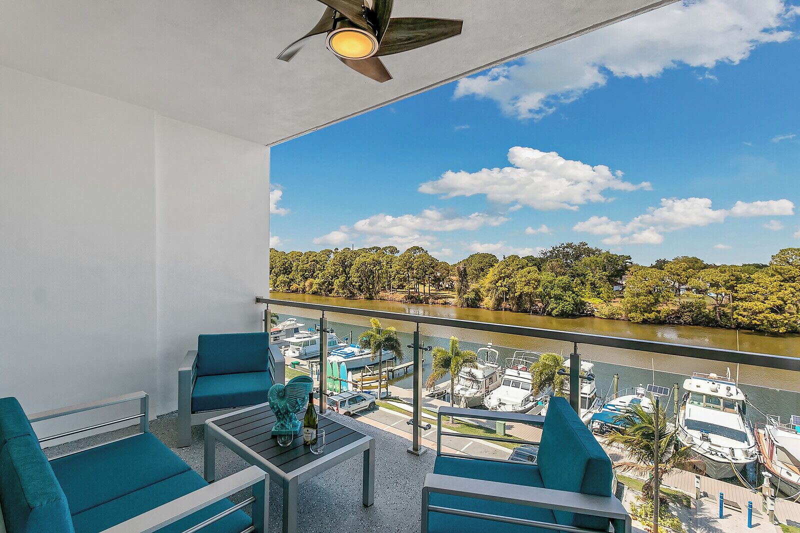 A balcony with teal chairs and a table, overlooking a marina with boats and a river.