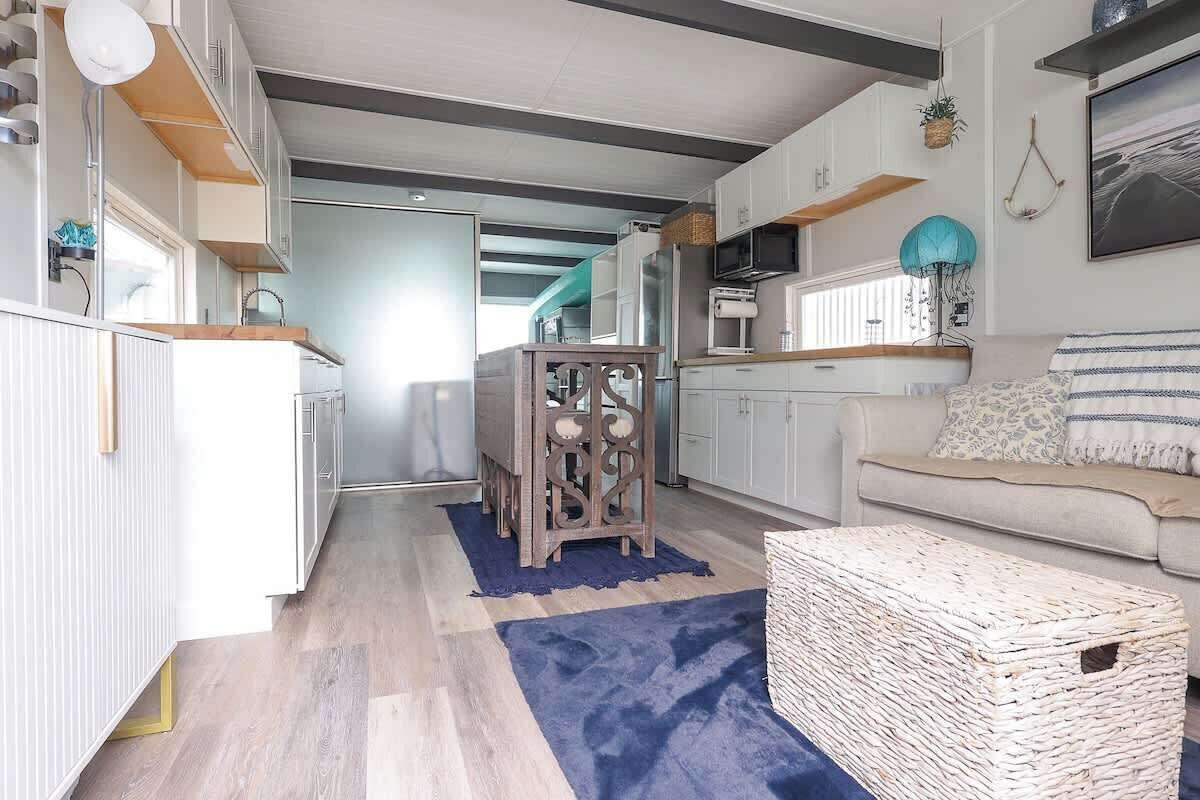 A modern kitchen with white cabinets, a wooden dining table, and a blue rug.