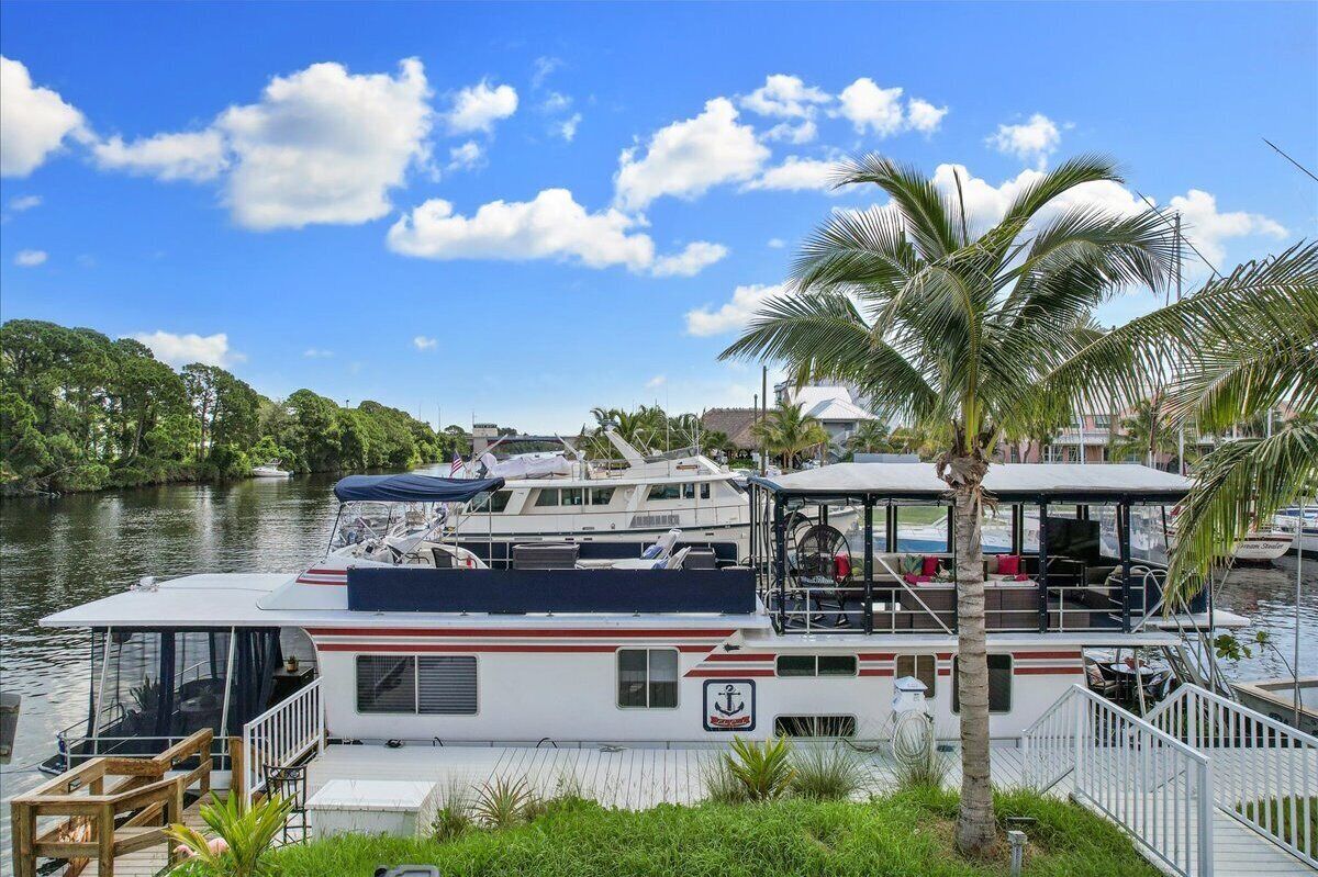 Une péniche amarrée, dotée d’une terrasse couverte, d’un petit espace salon extérieur et offrant une vue sur l’eau et les arbres.