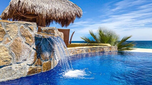 Ein Pool mit Wasserfall, eine Struktur mit einem Strohdach und eine Palme.
