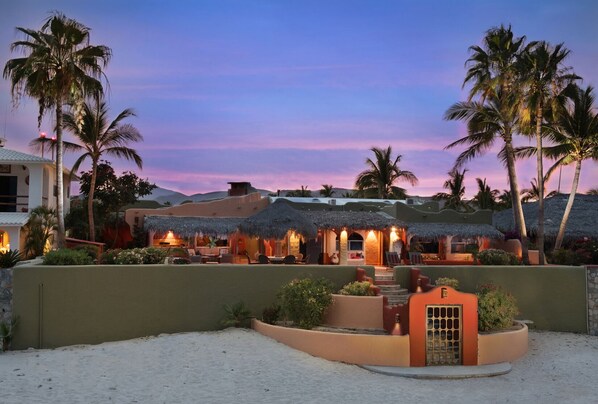 A resort with thatched-roof structures, palm trees, and a sandy beach.