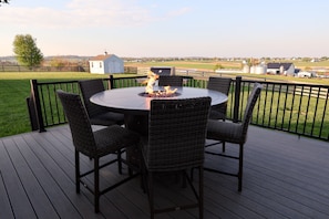 Une terrasse dotée d’une table ronde et de chaises, d’un foyer et offrant une vue sur un paysage rural.