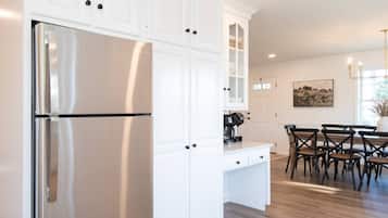 A kitchen with white cabinetry, a stainless steel refrigerator, and a dining area with wooden chairs and a table.