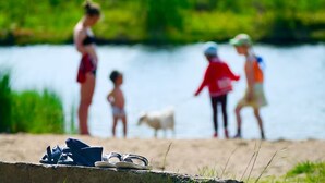 Une famille au bord d’un lac, avec une rive en béton, et une paire de sandales au premier plan.