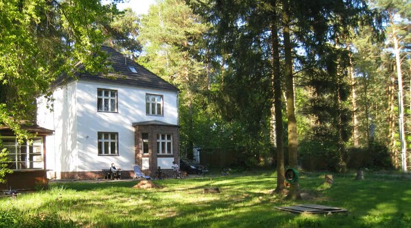 Ein zweistöckiges Haus mit weißer Fassade, umgeben von einem Rasen und Bäumen.