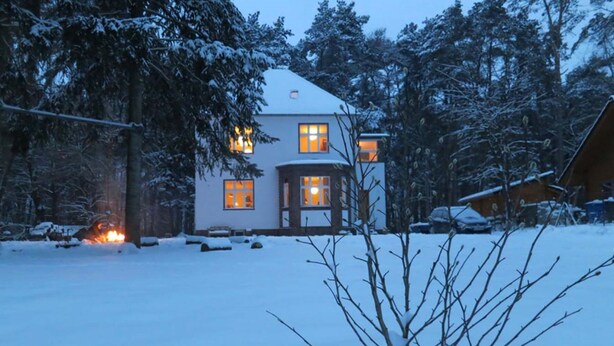 Une maison recouverte de neige, avec de nombreuses fenêtres et un feu visible au premier plan.