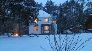 Ein mit Schnee bedecktes Haus mit vielen Fenstern und einem sichtbaren Kamin im Vordergrund.