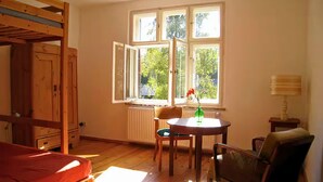 Une chambre avec un lit superposé, une table avec une chaise, une fenêtre donnant sur des arbres et une lampe sur une table d’appoint.