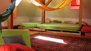 Ein Schlafsaalzimmer mit zwei Etagenbetten, einer Hängematte, einem grünen Schlafsofa und einem gemusterten Teppich.