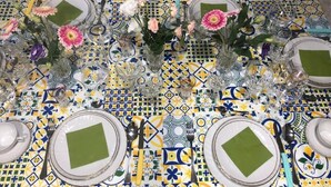 Una mesa dispuesta con platos, cubiertos y centros de mesa florales sobre un mantel estampado.