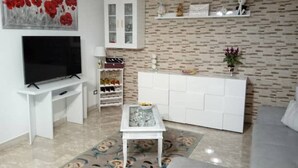 Un salón con televisor de pantalla plana, mueble blanco para equipo audiovisual, una mesa de centro y una alfombra estampada.
