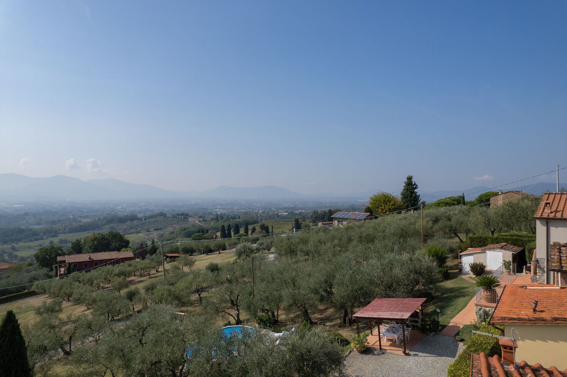 A villa with a pool, olive trees, and a view of distant mountains.
