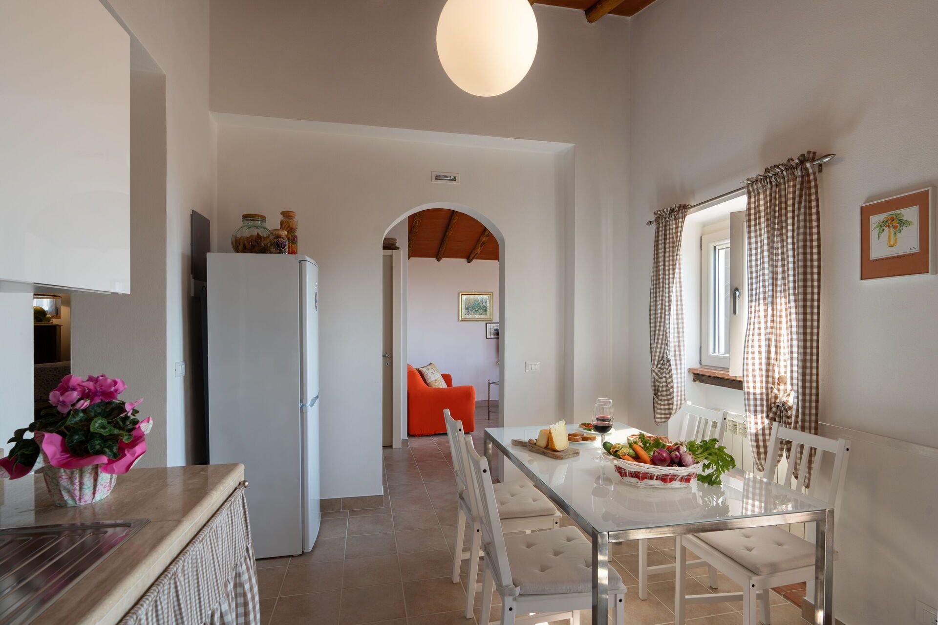A modern kitchen with white appliances, a dining table with chairs, and a view of a living area with a sofa and a window with curtains.