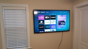 Ein Flachbildfernseher an der Wand, der eine Streaming-Oberfläche mit verschiedenen Sendern zeigt.