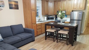 Eine moderne Küche mit Holzausstattung, einem Essbereich mit zentraler Kochinsel und einem grauen Sofa.