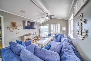 A living room with a large sectional sofa, a flat-screen TV, a ceiling fan, and a decorative wall piece.