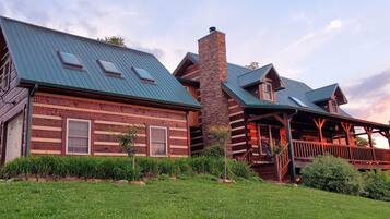 Cozy cabin-style building with a stone chimney and green roof, featuring multiple windows and a covered porch.