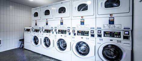 Una hilera de lavadoras blancas de carga frontal con paneles de control digital, dispuestas en un establecimiento de lavandería comercial.