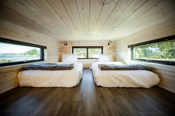 A cabin with two beds, wooden walls, and large windows overlooking a natural landscape.