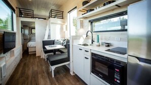 A compact kitchen with a dining area, a built-in oven, and a TV. - Dune Cabin - The Dune Cabin is well-appointed and uniquely designed and comfortably sleeps 6 guests. Private bedroom with queen bed, open loft with twin beds, and dinette that converts to a full size bed (Coos Bay)