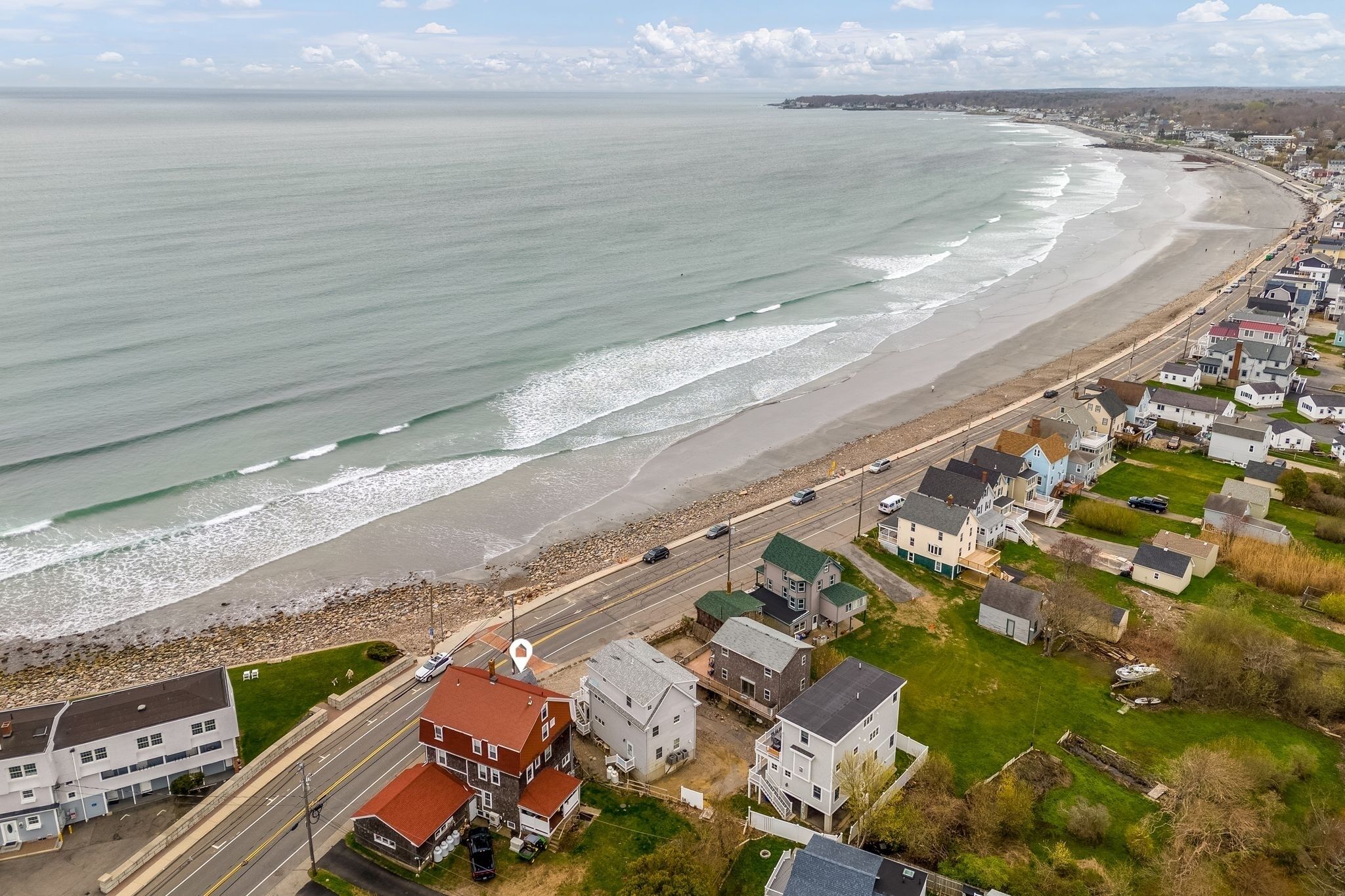 Ein Küstenwohngebiet mit Häusern entlang des Strandes, einer Straße und freiem Blick auf den Ozean.