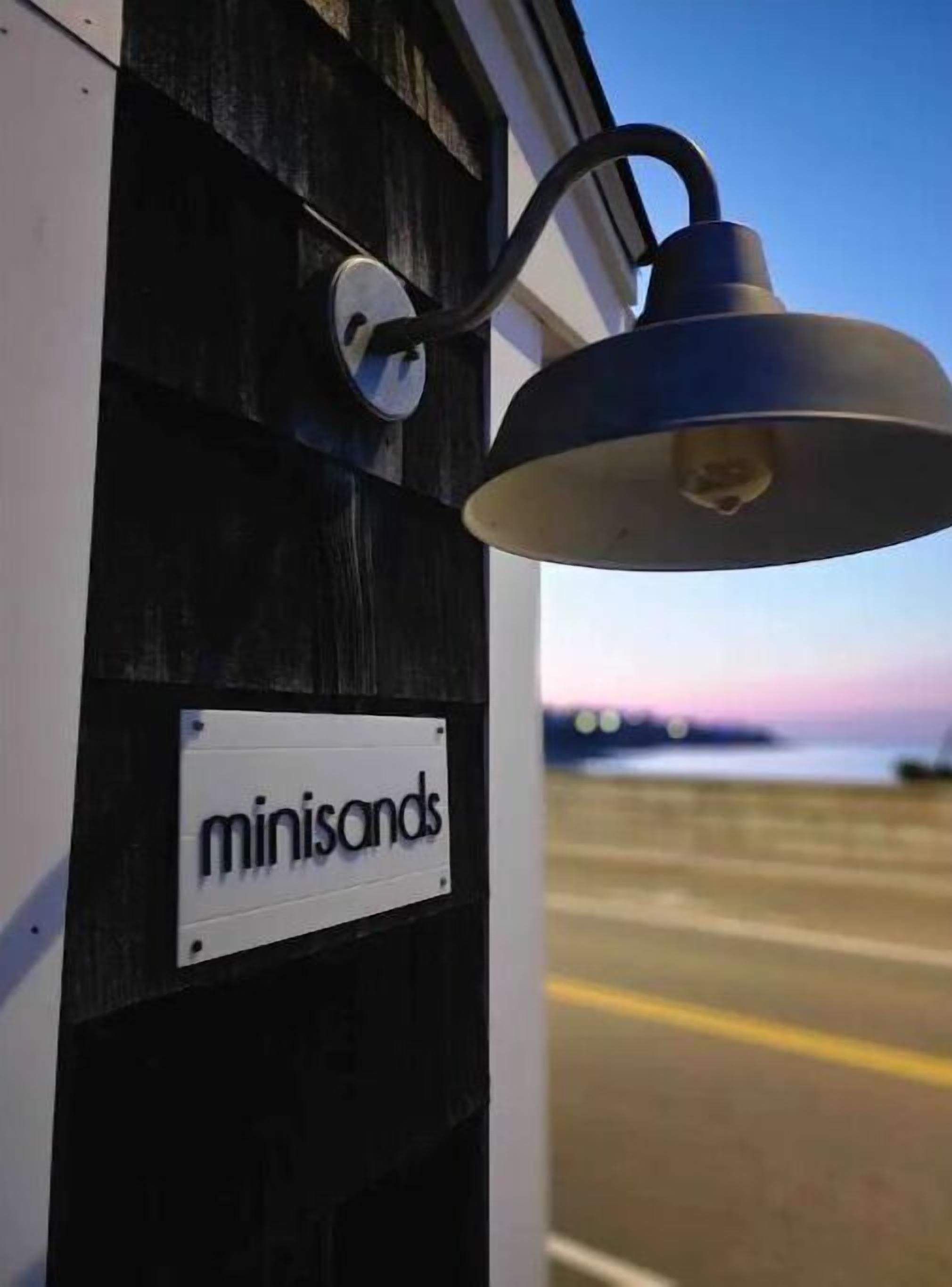 Ein Schild mit der Aufschrift "minisands" an einem Gebäude mit schwarzer Fassade und einer hängenden Lampe.