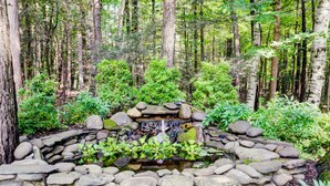 A natural stone pond surrounded by rocks and greenery, with a waterfall feature in the center. - Mid-Century Modern House Convenient to All that Woodstock has to Offer. (Woodstock)